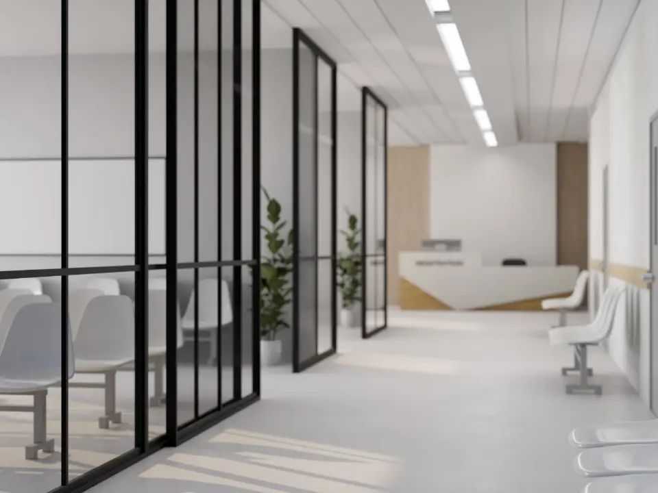 Couloir de cabinet médical moderne avec cloisons vitrées noires, chaises blanches et comptoir d'accueil lumineux.