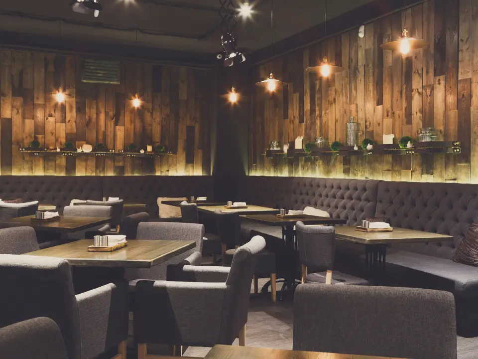 Salle de restaurant chaleureuse avec mur en bois, banquettes capitonnées gris foncé et suspensions lumineuses.