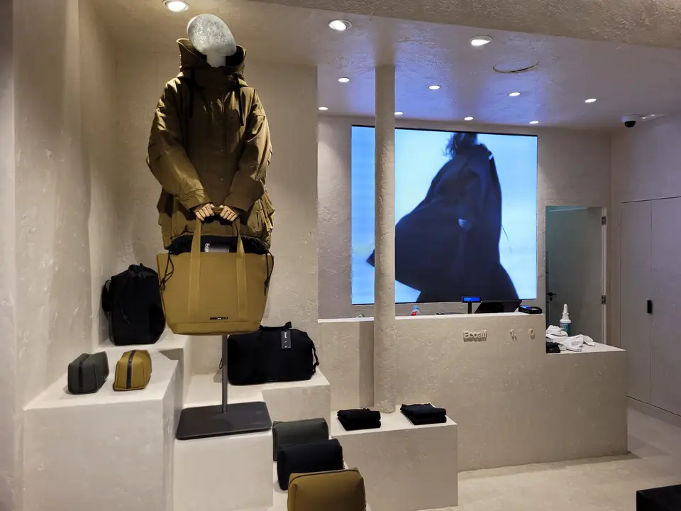 Podio, maniquí y marroquinería frente a la pantalla de la marca