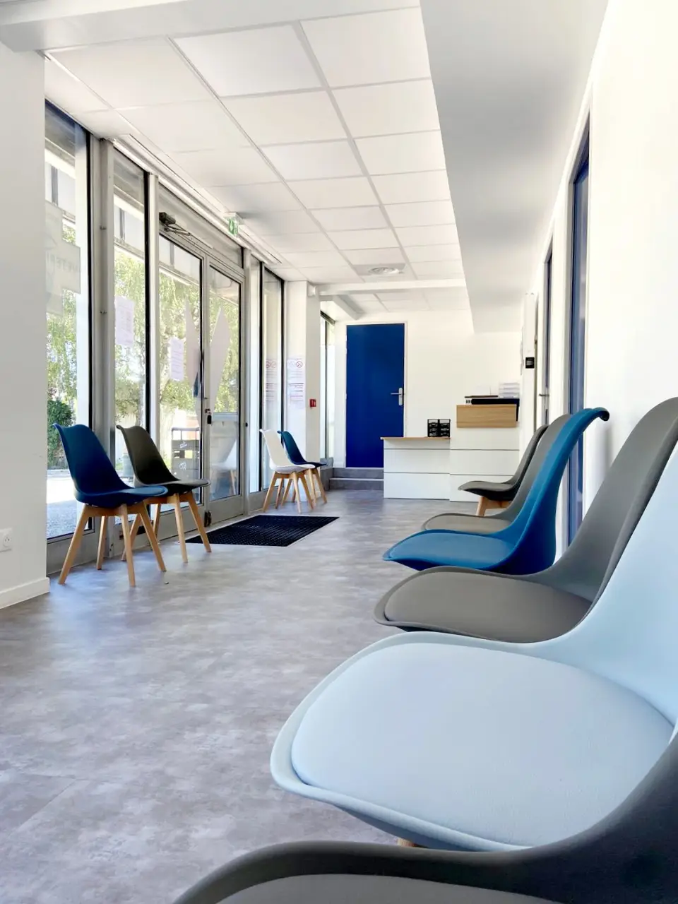 Salle d'attente d'une clinique vétérinaire avec des chaises modernes aux couleurs douces, sol gris et murs blancs lumineux.
