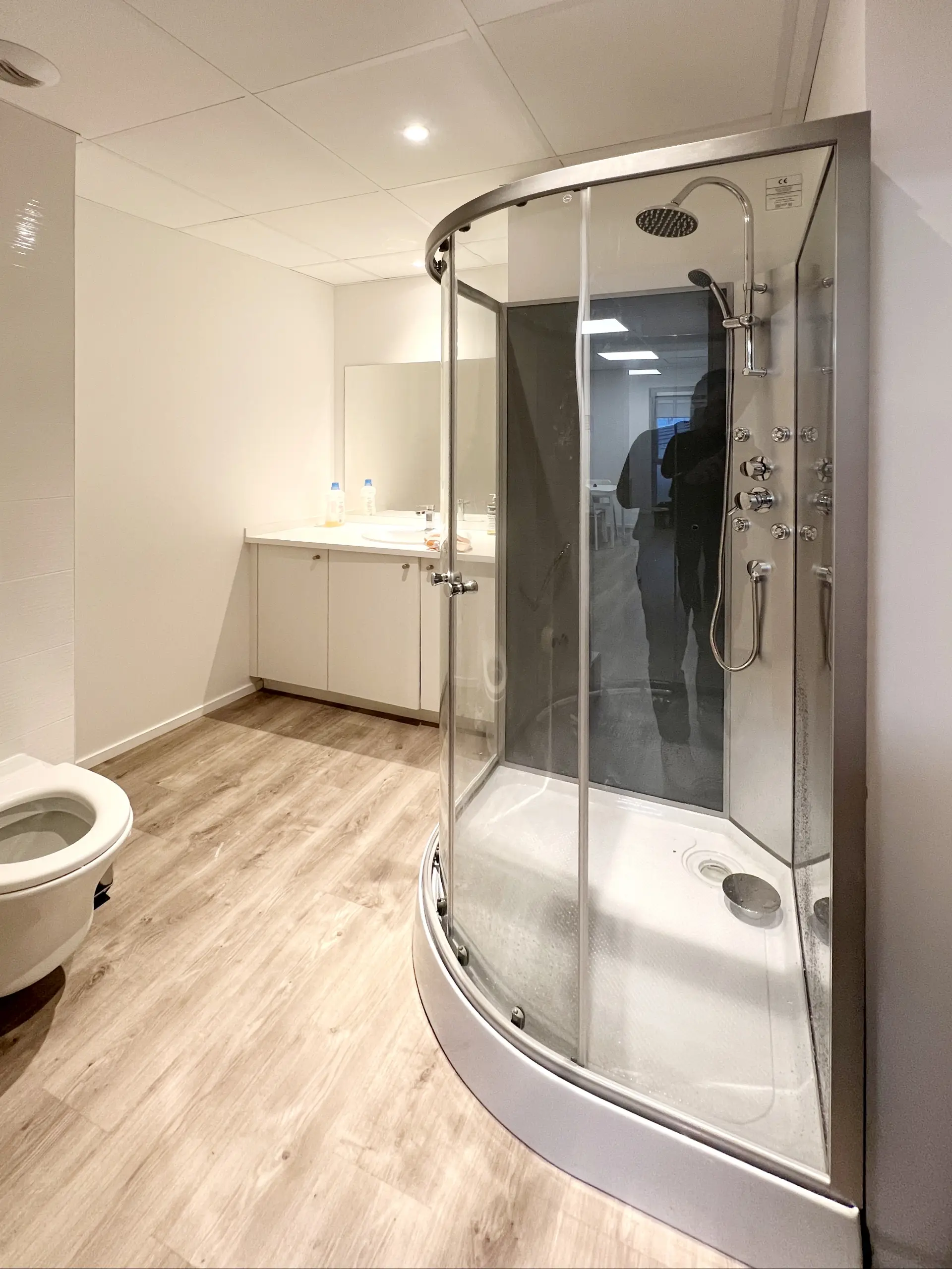 Salle de bain moderne et propre, équipée d'un WC, d'un lavabo avec miroir et d'une douche de plain-pied.