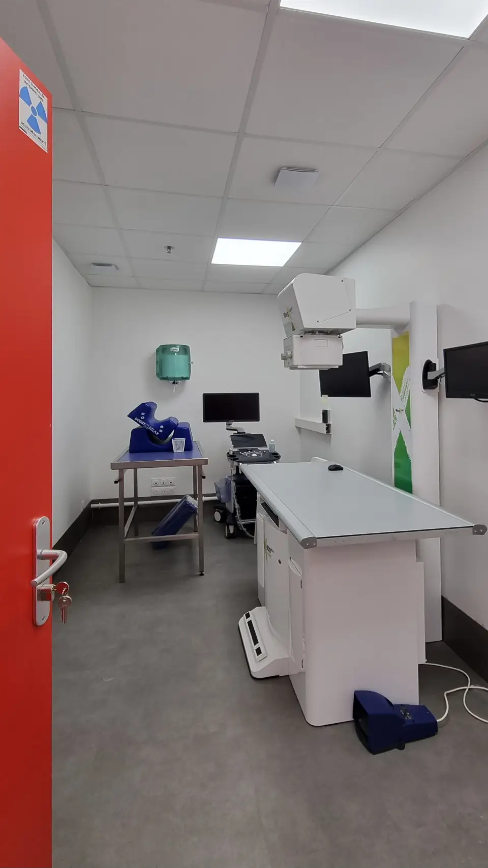 Une salle d'examen vétérinaire moderne avec une table d'opération, des écrans et un équipement à rayons X.