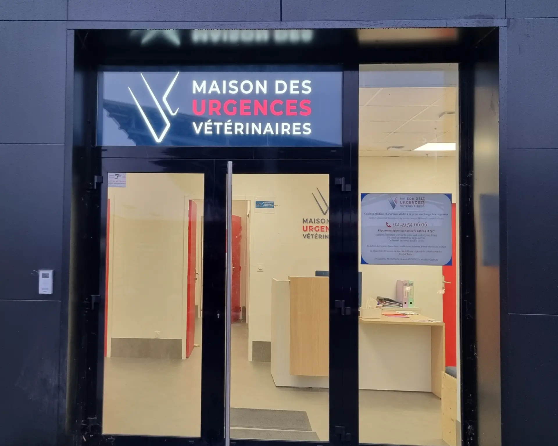 Façade vitrée noire et murs gris d'une clinique vétérinaire. L'enseigne lumineuse affiche "Maison des Urgences Vétérinaires".