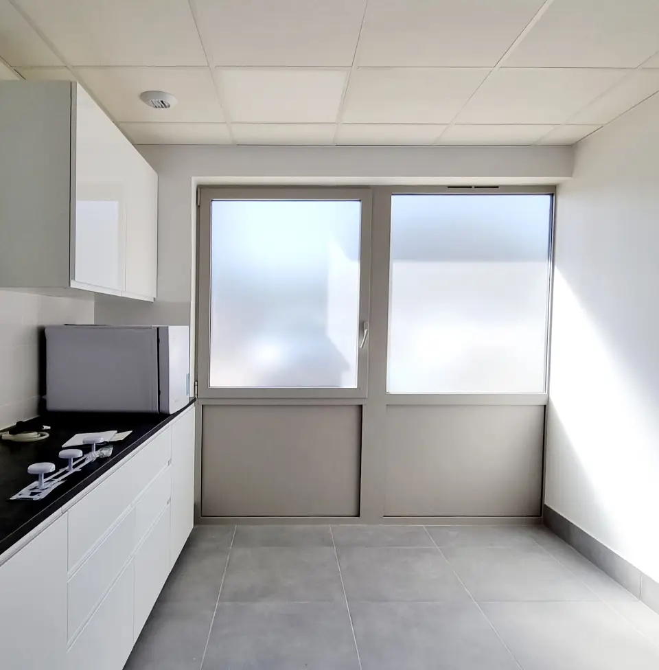 Coin cuisine lumineux d'une clinique vétérinaire moderne avec mobilier blanc, plan de travail noir, et grande fenêtre givrée.