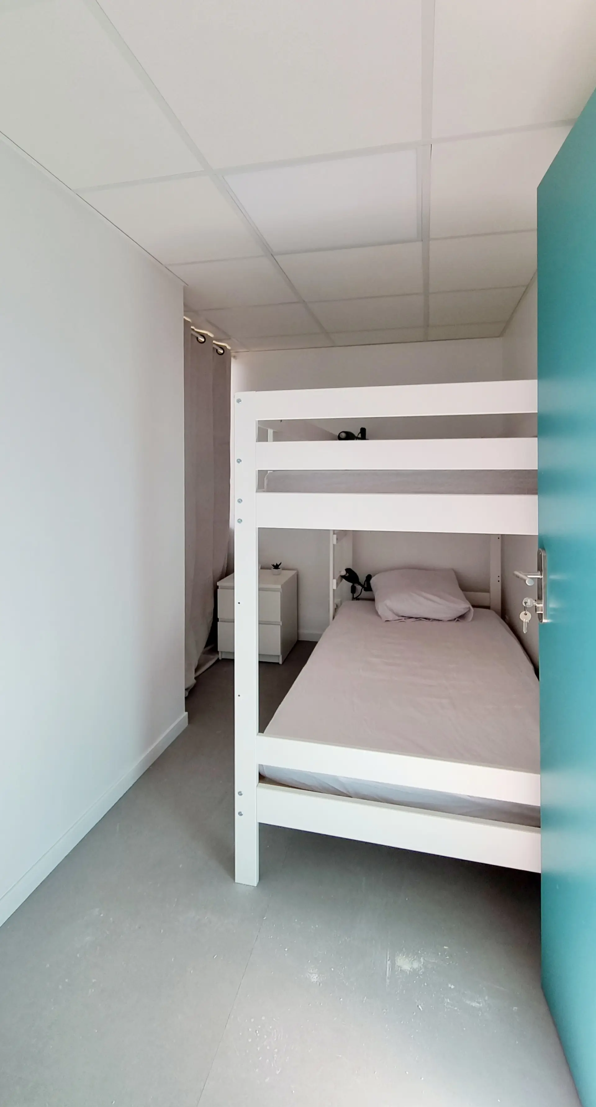 Chambre avec lit superposé blanc, murs blancs et porte turquoise vif dans un espace professionnel moderne.