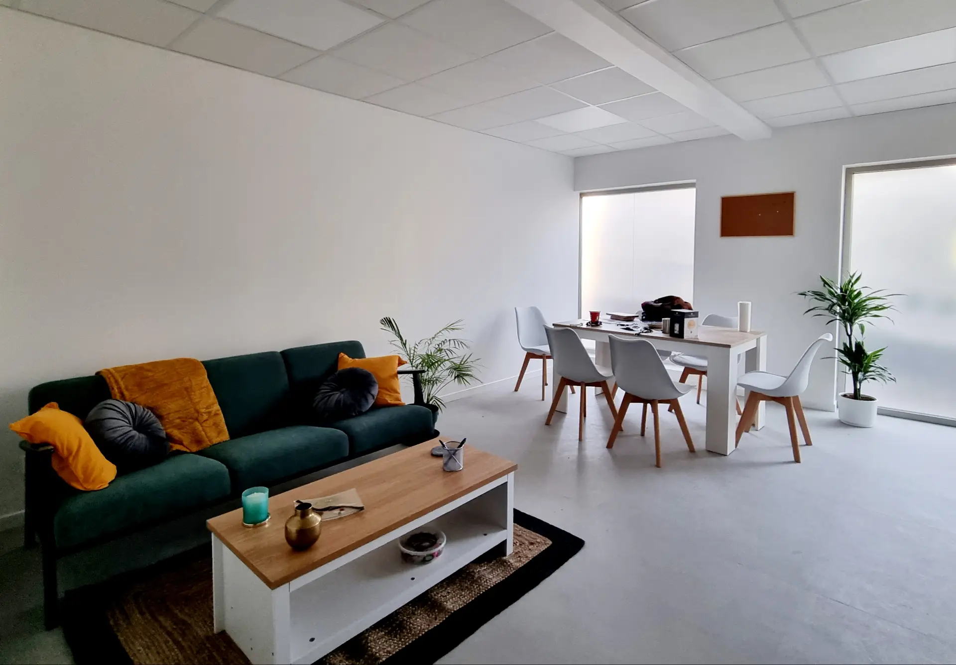 Un espace d'accueil moderne et lumineux avec un canapé vert en velours, une table basse en bois et un coin repas.