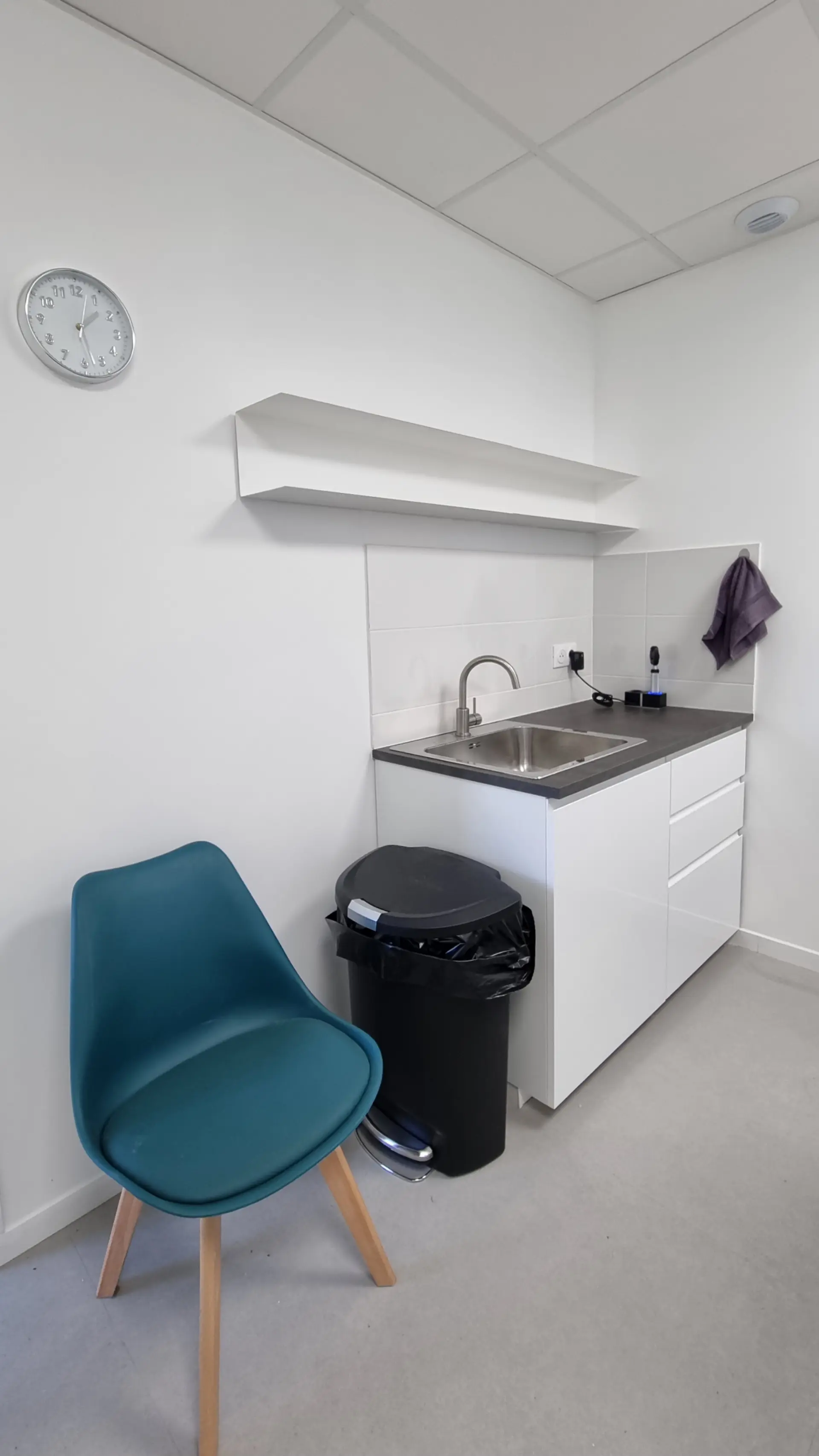 Un coin cuisine moderne et épuré avec un évier en inox, des placards blancs, et une chaise turquoise design.