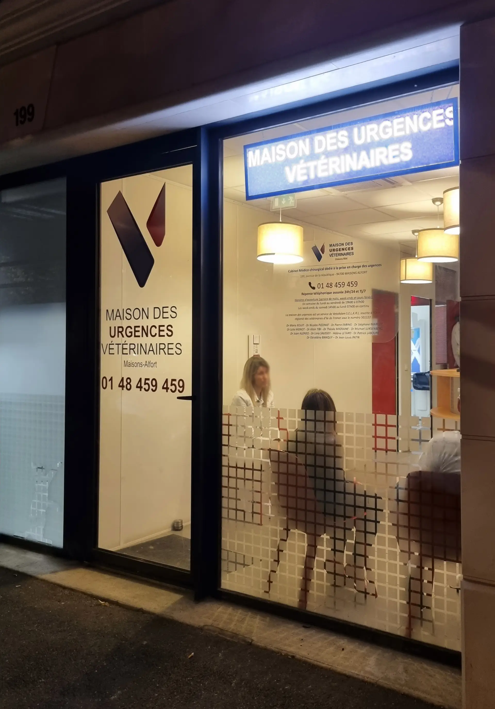 Façade vitrée illuminée d'une clinique vétérinaire de nuit, logo et textes lisibles, lumière chaude intérieure.