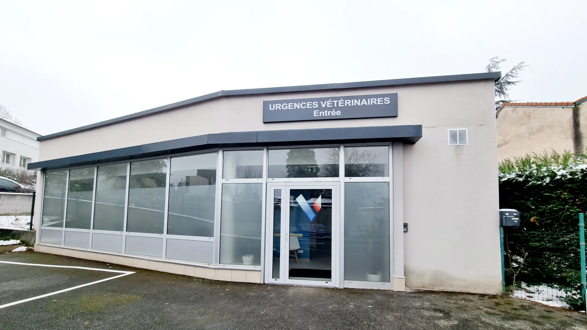 Bâtiment d'une clinique vétérinaire de plain-pied, façade crème, grandes baies vitrées et enseigne noire « Urgences Vétérinaires ».