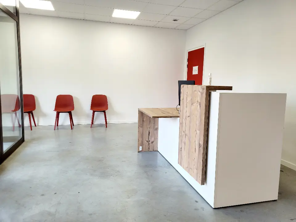 Zone d'accueil et d'attente d'une clinique vétérinaire. Banque d'accueil en bois clair texturé et blanc, chaises rouges, porte rouge vif.