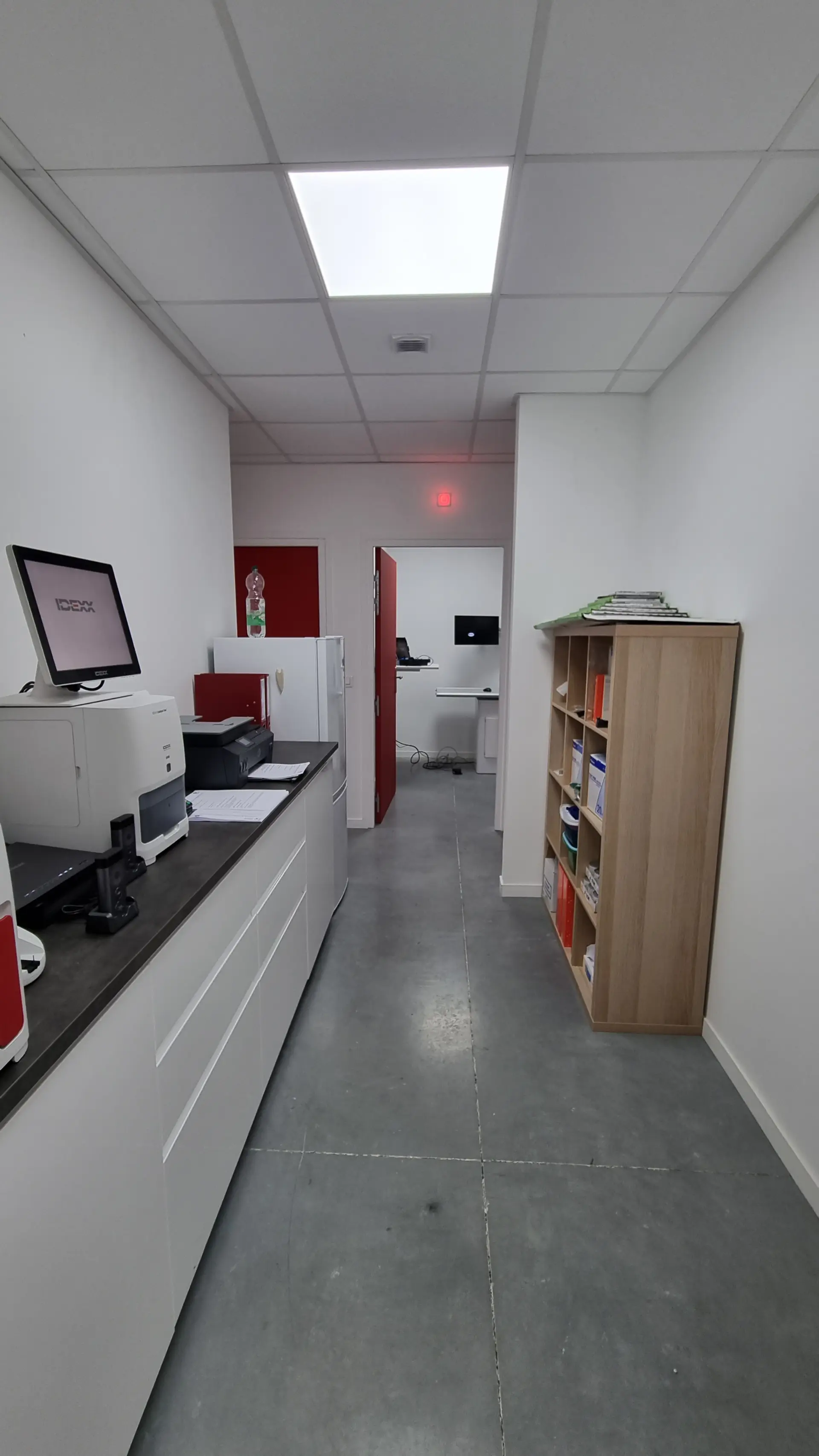 Un espace de travail moderne avec un sol en béton, un comptoir blanc, des meubles de rangement clairs et un écran d'ordinateur.