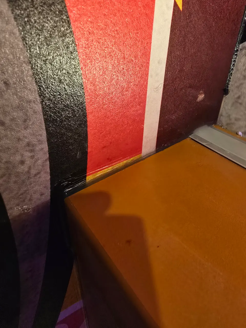 Gros plan sur un revêtement de sol coloré et texturé en rouge, noir et marron, avec un mur saumon et une lumière chaleureuse.